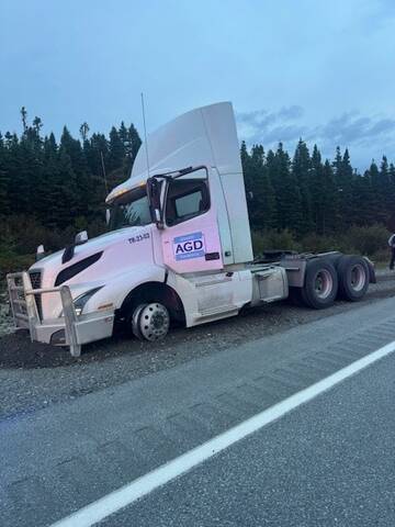 A transport truck is parked on the gravel shoulder of a roadway with its front end dug into the gravel and a flattened front driver side tire.