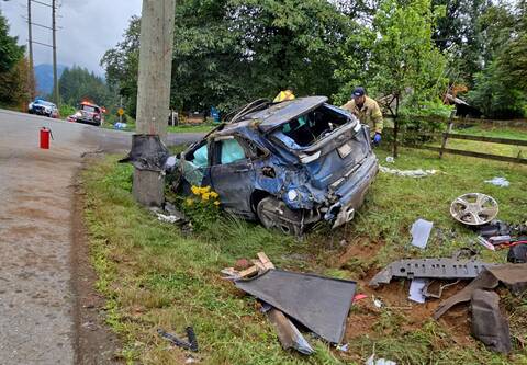 Photo of a blue car crashed into a utility pole, with firefighters working near it.