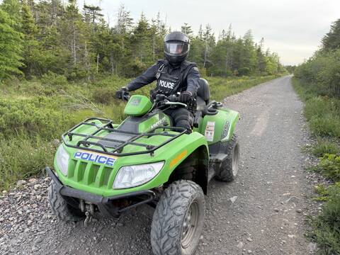 a uniformed RCMP officer wearing a helmet, and sitting on a bright green all-terrain vehicle with RCMP decals.
