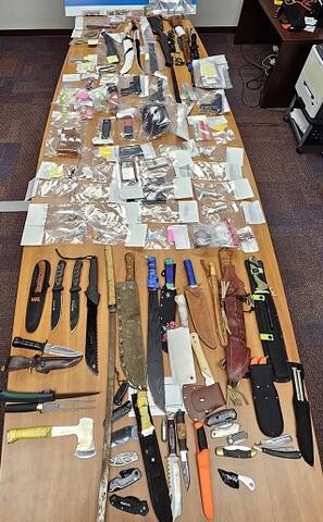 A number of items, including knives, firearms, drugs and drug paraphernalia, are displayed on a table.