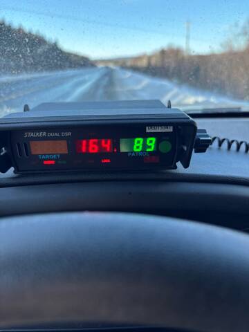 A police speed radar from inside a police vehicle shows a speed of 164, and a view of snow and ice covered winter roads in front of the police vehicle.