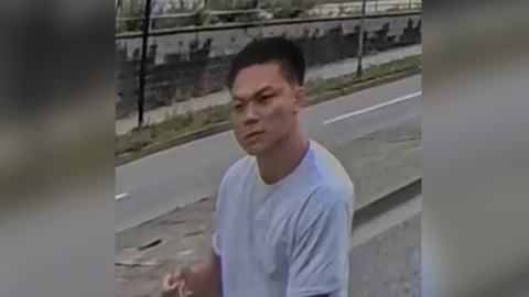 Asian male in his twenties, wearing a white t-shirt standing in the street.