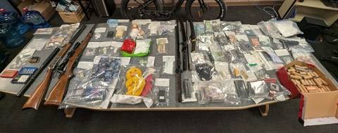 A display of seized items spread onto a table including drugs, guns, cash and other weapons and ammunition.