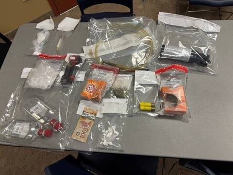 A photo of cash, clear evidence bags with suspected drugs and other items inside are spread out on a gray table.