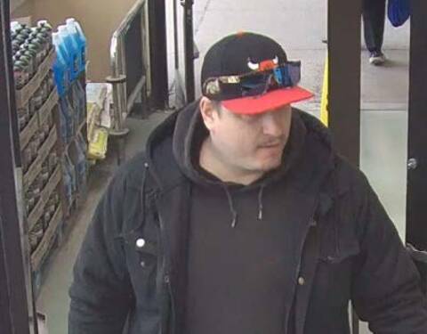 Surveillance image of suspected shoplifter in Prince George wearing a black and red Chicago Bulls cap, sunglasses on the brim, black hoodie and black jacket.