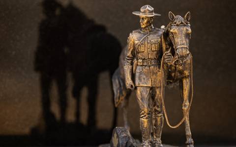 A bronze RCMP horse and rider figure on a granite stone with a shadow behind.