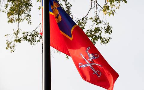 The Depot Division Ensign which is a flag that features cavalry swords and the lamp of knowledge on a red background.