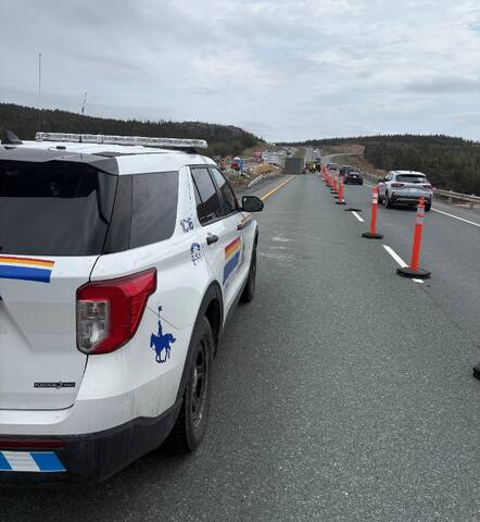 A fully marked RCMP police vehicle sits inside a highway construction zone, while vehicles pass in the right-hand lane. Construction crews are visible in the background.