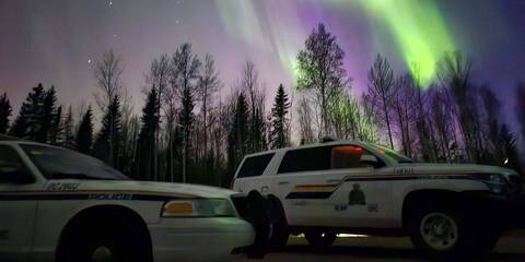 Photo of two police cars pictured in front of the Northern Lights in the sky.