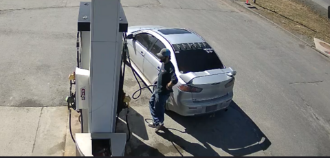 Surveillance image of male suspect with brown wavy hair and full beard pumping fuel into a vehicle at a Whitbourne gas station