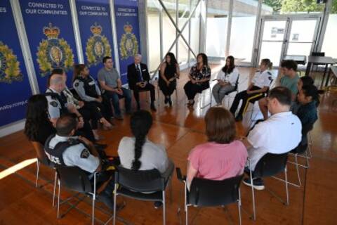 A group of people sit indoors in a circle in a building with RCMP logos