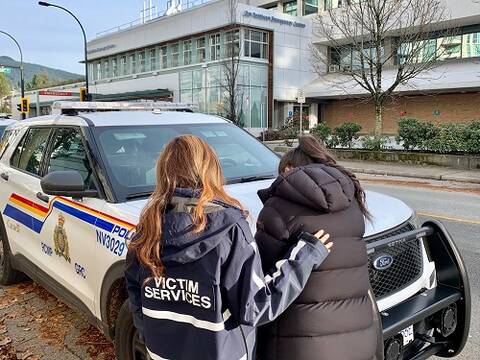 A Victim Services member consoling a person next to a police car