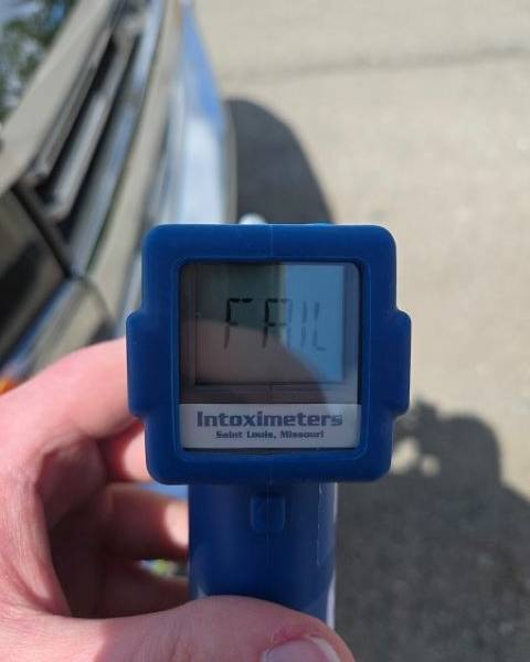 A blue roadside screening device with the word FAIL on it with a blurry silver bumper and the roadway in the background.