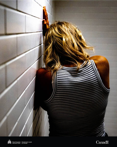 A woman is pictured, facing away and leaning against a white tiled wall with hand pressed against it.